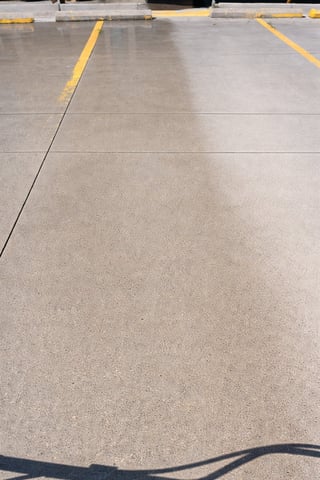 Empty parking lot with concrete surface, yellow painted parking spaces, and crack marks visible on asphalt