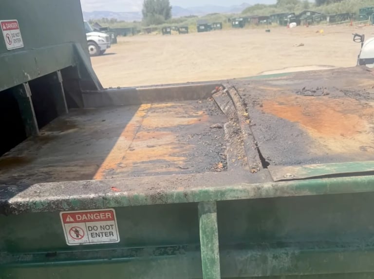 Interior of a green dumpster with danger warning signs, partially filled with dirt and debris at an outdoor lot