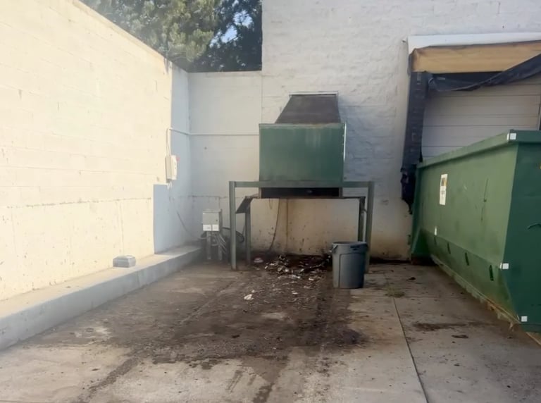 Industrial waste management area with dumpsters and green bins against white concrete walls