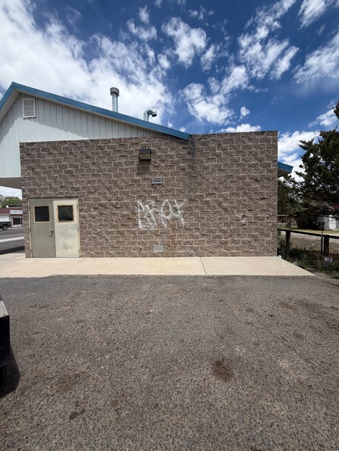Brown brick industrial building with white metal roof section and entrance door under blue sky with white clouds