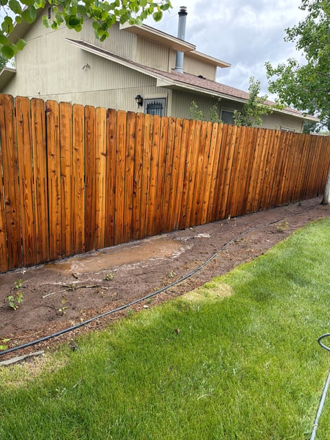 Wooden fence surrounding a residential property with a house and green lawn visible in the background