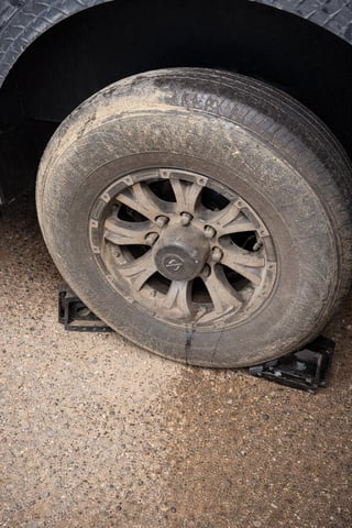 Close-up of a worn vehicle tire with dirt buildup on a gravel surface, supported by a jack