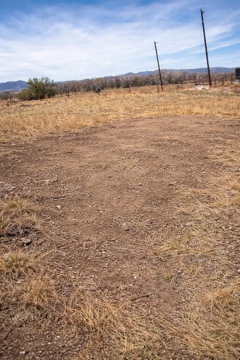Dry rural farmland with two wooden posts, bare trees, and mountains under a blue sky