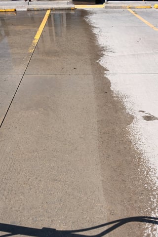 Wet concrete parking lot with yellow line markings and a dark hose in foreground