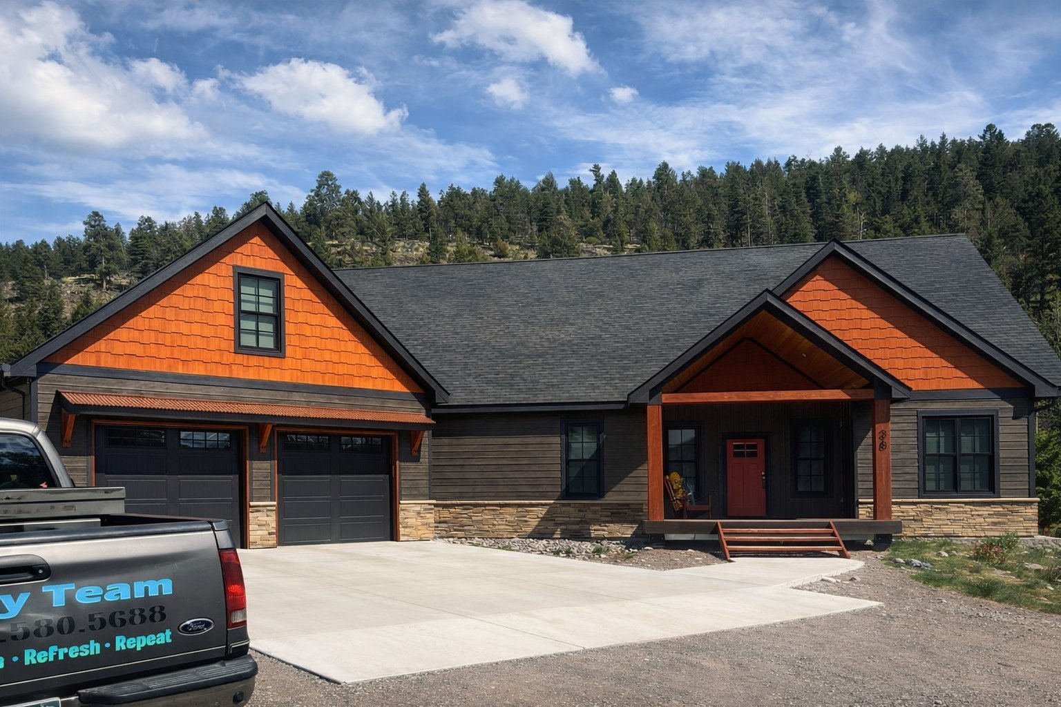 Modern residential home with orange and gray exterior, two-car garage, and forested background on sunny day