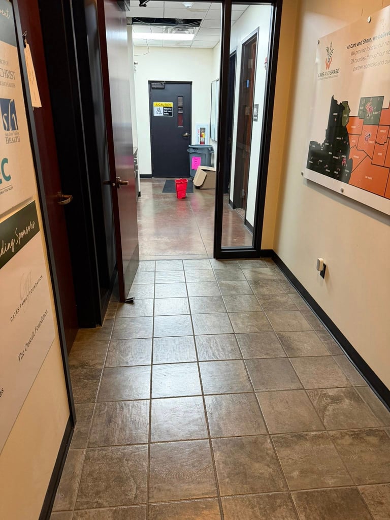 Interior hallway with tile flooring, dark doors on sides, and open doorway leading to office area with desk and equipment