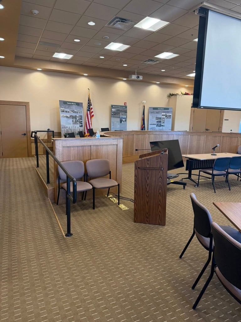 Interior of a courtroom with judges bench, American flag, witness chairs, and projection screen