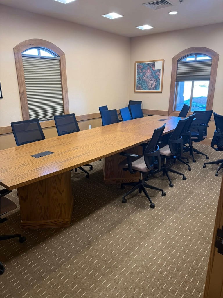 Modern conference room with long wooden table, black office chairs, arched windows with blinds, and recessed ceiling lights