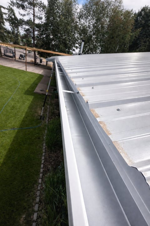 Close-up view of a white metal roof gutter along a residential building with green grass and trees in background