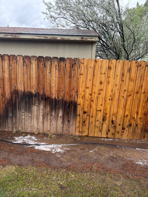 Weathered wooden fence with dark stains and deterioration, backed by a house and bare trees