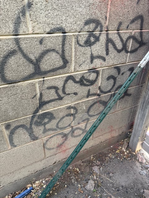 Concrete cinder block wall with black graffiti and a green metal pipe running horizontally across it
