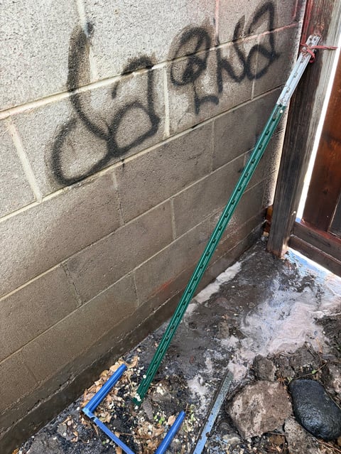 Concrete block wall with black graffiti and garden hose leaning against it on ground