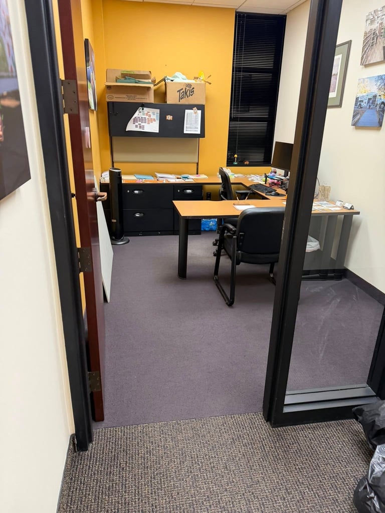 Small office workspace with yellow accent wall, black desk and chair, and storage shelves viewed from doorway entrance